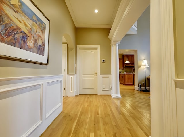 corridor featuring wainscoting, ornamental molding, light wood-style flooring, and decorative columns