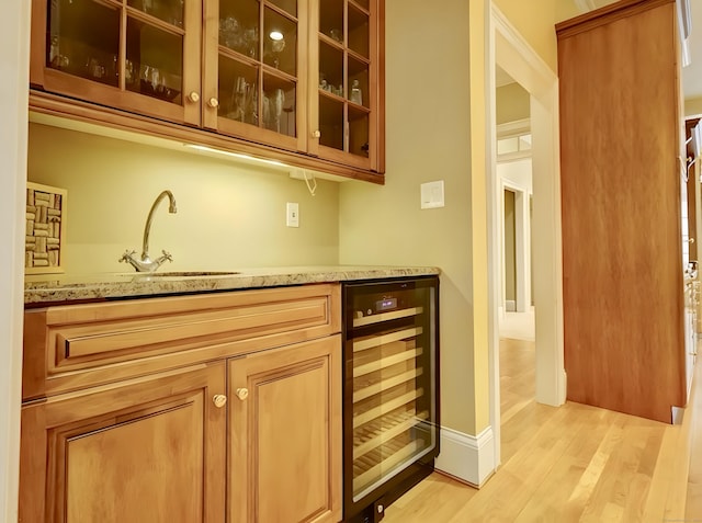 bar featuring baseboards, light wood-style flooring, a sink, indoor wet bar, and wine cooler