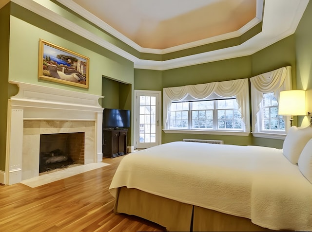 bedroom with a tiled fireplace, crown molding, multiple windows, and wood finished floors