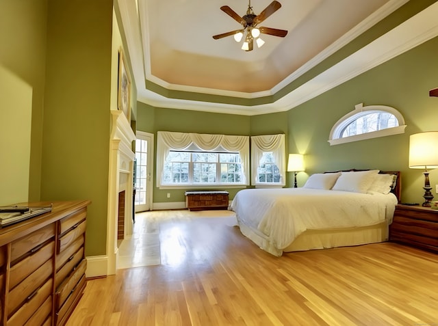 bedroom with a tray ceiling, light wood-type flooring, ornamental molding, and a fireplace