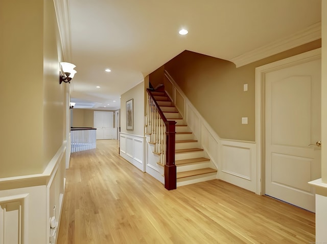 stairs featuring wood finished floors, a wainscoted wall, recessed lighting, crown molding, and a decorative wall