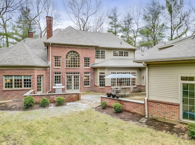 rear view of house featuring a patio, a yard, brick siding, and a chimney