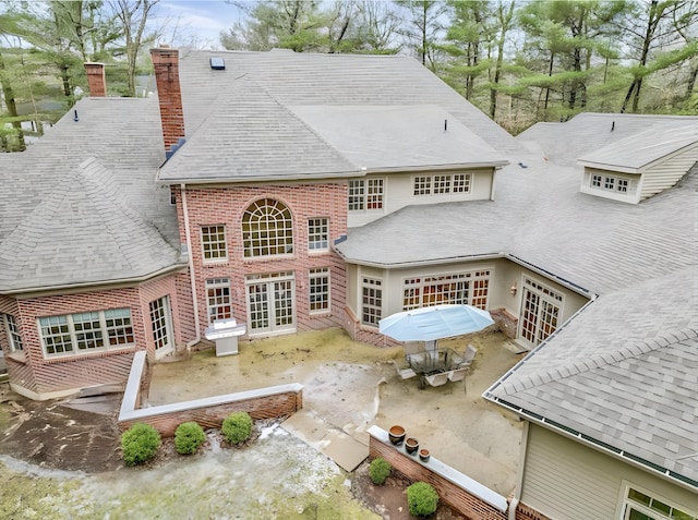 back of property with outdoor dining area, a chimney, french doors, a garage, and brick siding