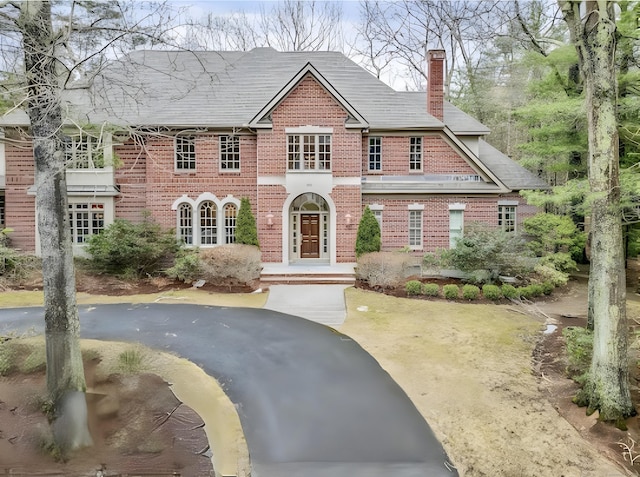 view of front of home featuring brick siding, a chimney, and aphalt driveway