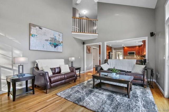 living room featuring light wood-style flooring, baseboards, and a towering ceiling