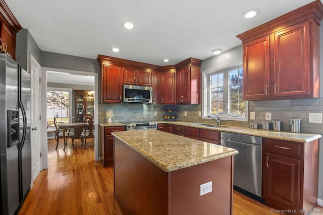 kitchen with a sink, backsplash, appliances with stainless steel finishes, light wood finished floors, and light stone countertops