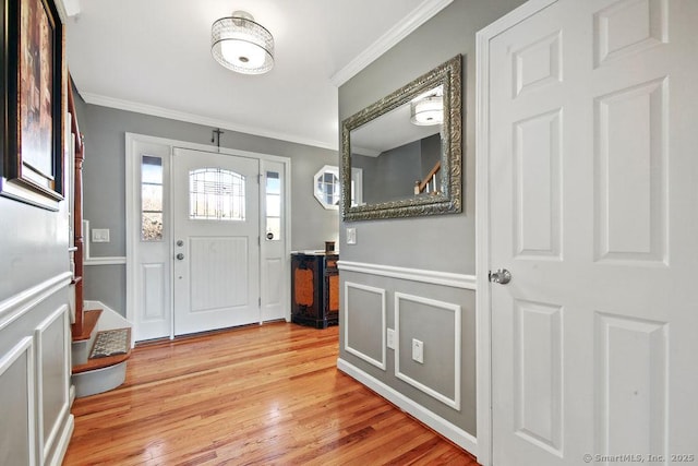 foyer entrance featuring a wainscoted wall, a decorative wall, light wood-type flooring, and ornamental molding