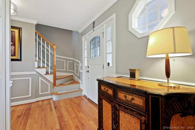 foyer entrance with stairway, light wood-style flooring, wainscoting, crown molding, and a decorative wall