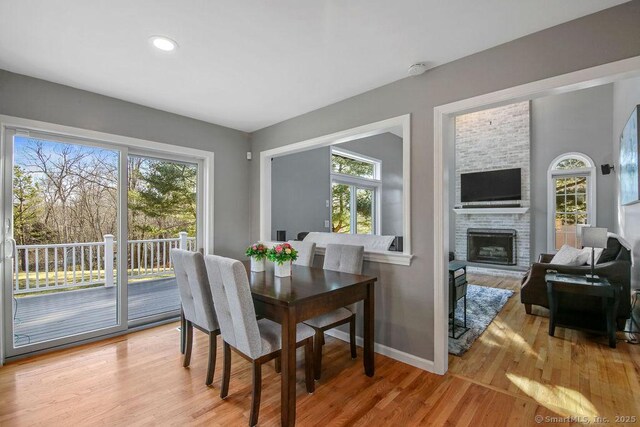 dining area with baseboards, plenty of natural light, a brick fireplace, and light wood-style flooring