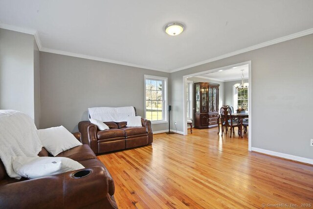 living room featuring a notable chandelier, baseboards, light wood-type flooring, and ornamental molding