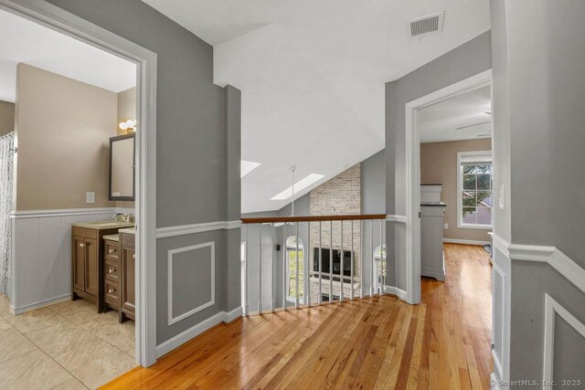 hallway featuring visible vents, a sink, wainscoting, lofted ceiling with skylight, and light wood-type flooring