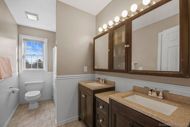 full bath featuring vanity, a wainscoted wall, tile patterned flooring, curtained shower, and toilet