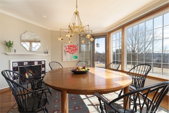 dining space featuring baseboards, a tile fireplace, wood finished floors, crown molding, and a chandelier