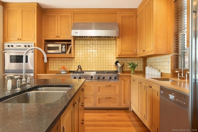 kitchen featuring stainless steel appliances, wall chimney range hood, a sink, and light wood-style flooring