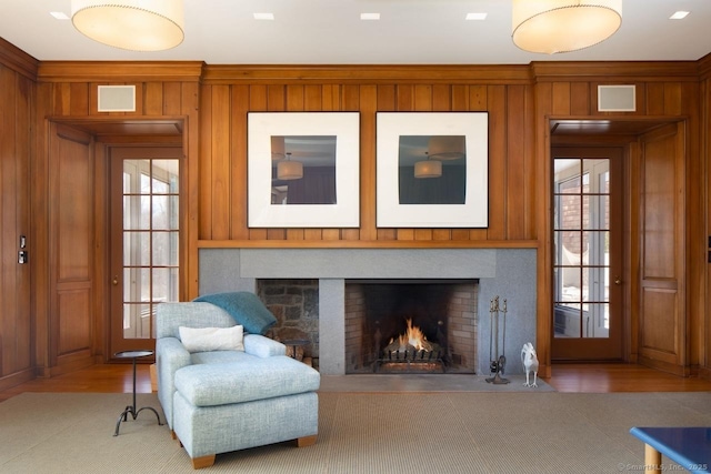 living area with a warm lit fireplace, wooden walls, a wealth of natural light, and wood finished floors