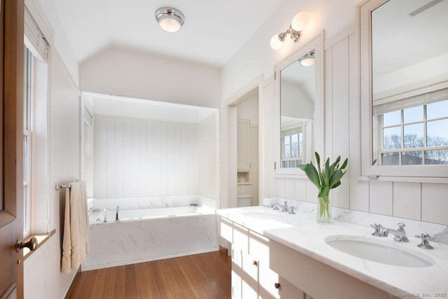 full bathroom with double vanity, a garden tub, a sink, and wood finished floors