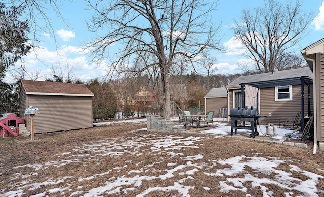 yard layered in snow featuring a storage shed, an outbuilding, a patio area, and fence