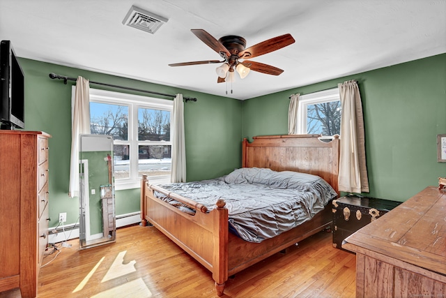 bedroom featuring a baseboard heating unit, light wood-style floors, visible vents, and ceiling fan