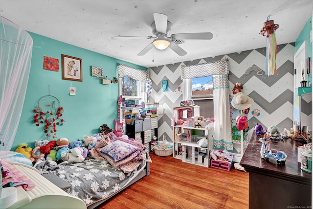 bedroom with a ceiling fan, wood finished floors, an accent wall, and wallpapered walls