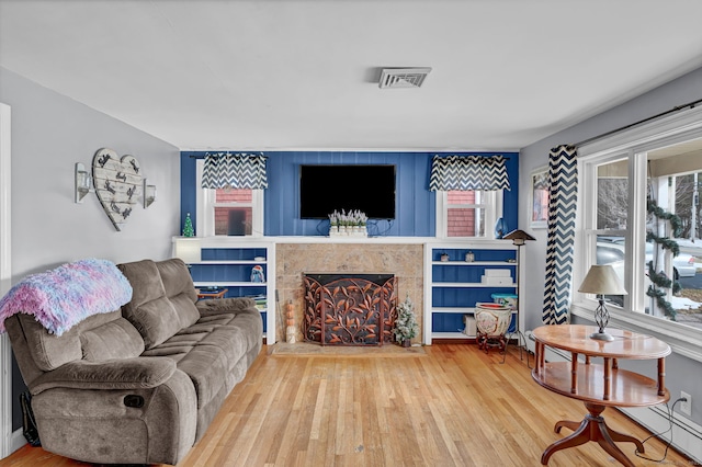 living room featuring a tiled fireplace, wood finished floors, visible vents, and a baseboard radiator