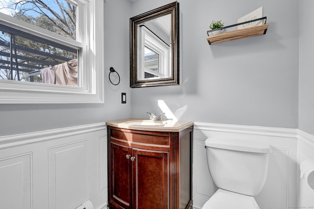 bathroom featuring a wainscoted wall, toilet, a healthy amount of sunlight, and vanity