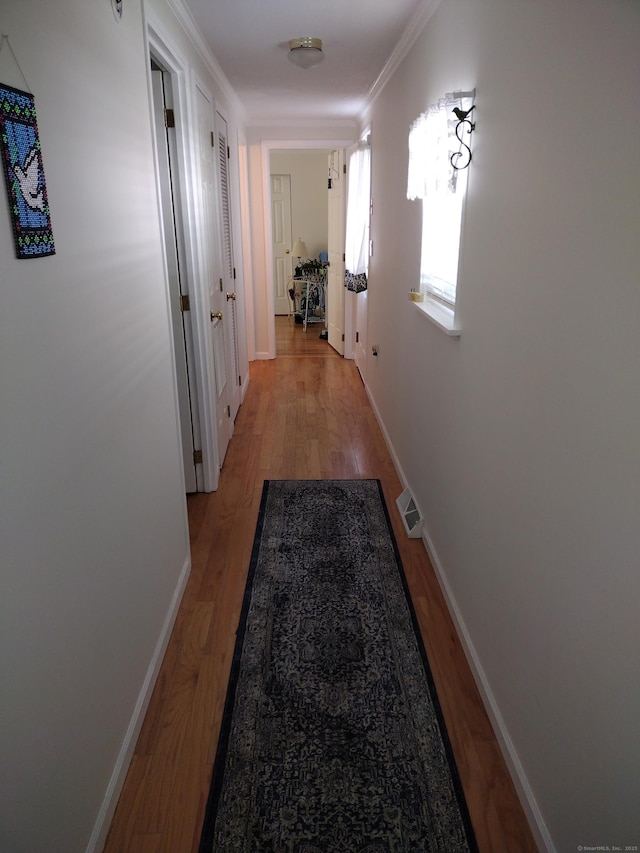 corridor with baseboards, ornamental molding, visible vents, and light wood-style floors