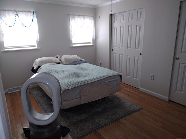 bedroom with visible vents, baseboards, wood finished floors, crown molding, and a closet