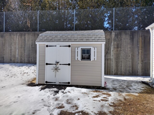 snow covered structure with fence, an outdoor structure, and a shed