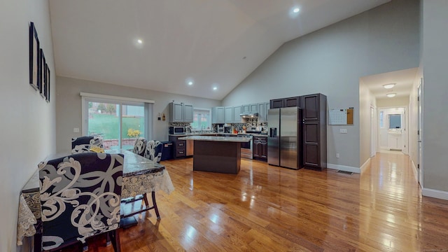 kitchen featuring high vaulted ceiling, light wood-style flooring, light countertops, appliances with stainless steel finishes, and a center island