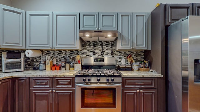 kitchen with light stone countertops, under cabinet range hood, tasteful backsplash, and stainless steel appliances