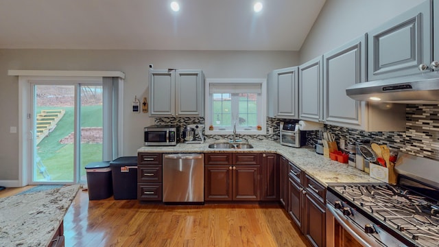 kitchen featuring appliances with stainless steel finishes, a sink, light stone countertops, and light wood-style floors