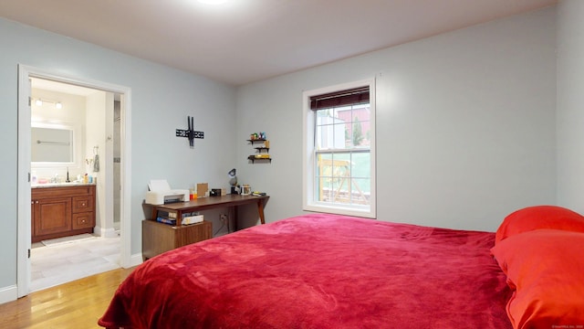 bedroom with light wood-style floors, baseboards, and ensuite bathroom