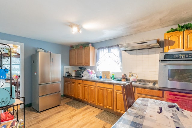 kitchen featuring decorative backsplash, light wood-style floors, stainless steel appliances, under cabinet range hood, and a sink