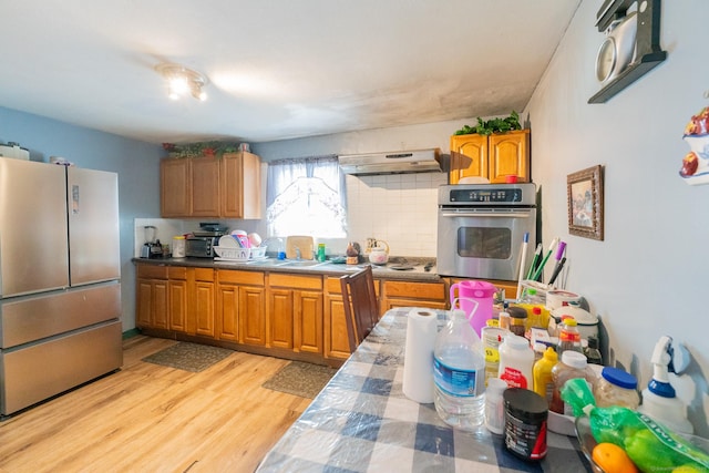 kitchen featuring under cabinet range hood, appliances with stainless steel finishes, light wood-type flooring, backsplash, and brown cabinetry