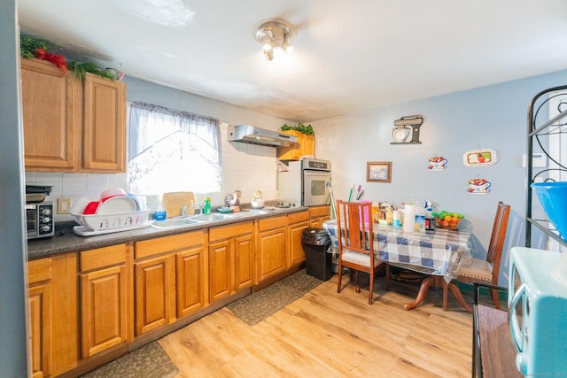 kitchen with light wood finished floors, white microwave, stainless steel oven, a sink, and under cabinet range hood