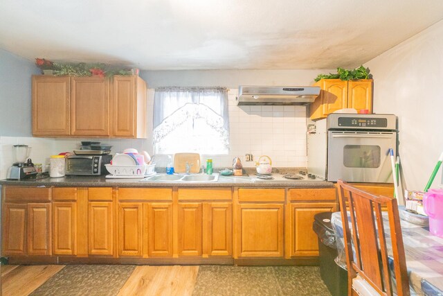 kitchen featuring light wood finished floors, white electric stovetop, oven, under cabinet range hood, and a sink