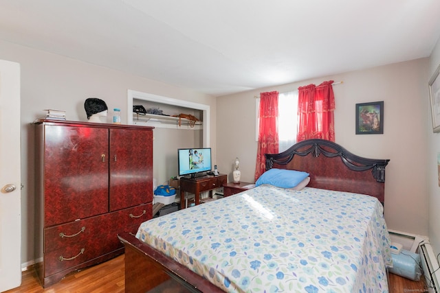 bedroom with baseboard heating and wood finished floors