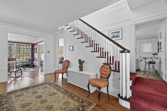 entrance foyer featuring ornamental molding, a decorative wall, parquet flooring, and stairs