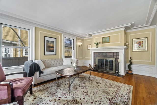 living room with ornamental molding, a tiled fireplace, wood finished floors, and a decorative wall