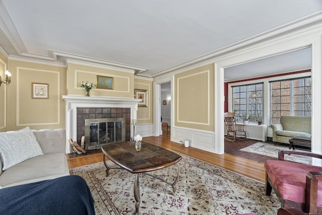 living area featuring ornamental molding, wood finished floors, a tile fireplace, and a decorative wall