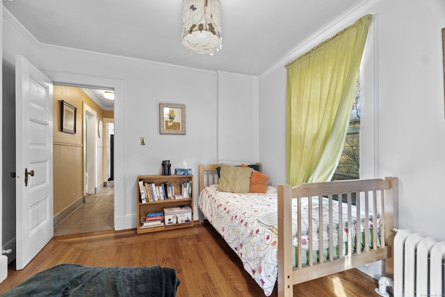 bedroom with crown molding, radiator heating unit, and wood finished floors