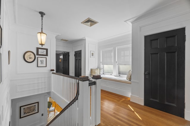 corridor with a decorative wall, visible vents, an upstairs landing, light wood finished floors, and crown molding