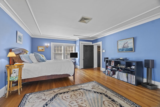 bedroom featuring baseboards, wood finished floors, visible vents, and crown molding