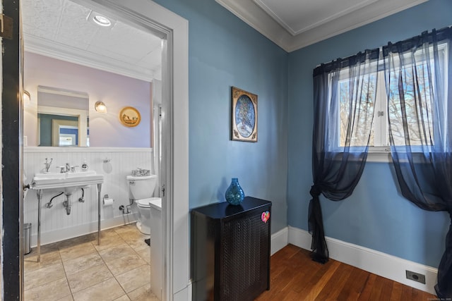 bathroom featuring baseboards, wainscoting, toilet, wood finished floors, and crown molding