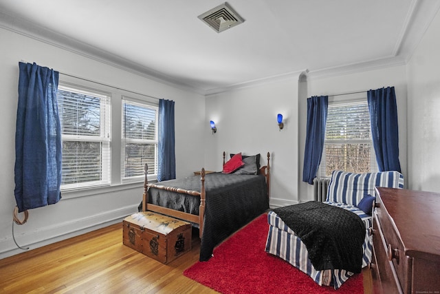 bedroom with ornamental molding, multiple windows, wood finished floors, and visible vents