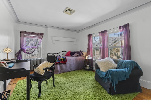 bedroom featuring visible vents, radiator heating unit, and wood finished floors