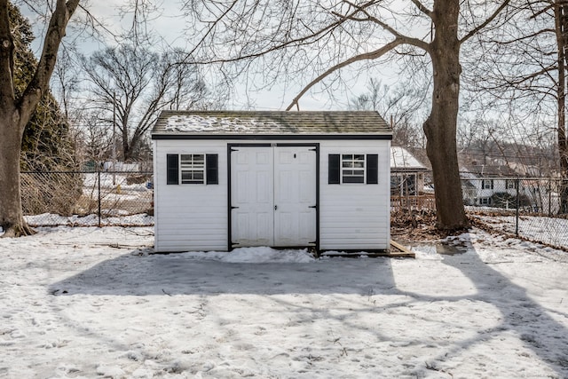 snow covered structure featuring an outbuilding, a storage unit, and fence