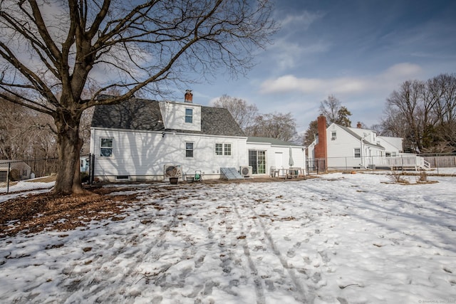 snow covered house with a shingled roof, fence, and a chimney