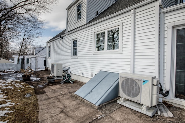 view of side of home with a shingled roof, ac unit, fence, and a gate