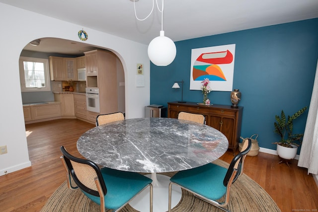 dining area with light wood-style flooring, arched walkways, and baseboards